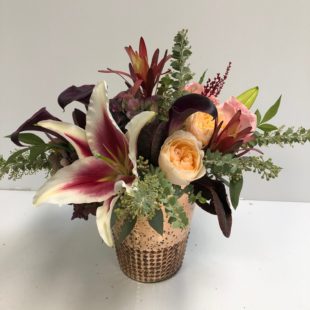 Garden Palisade flower arrangement with roses and lilies arranged in a unique vase, complemented by protea, eucalyptus, and a variety of other greens